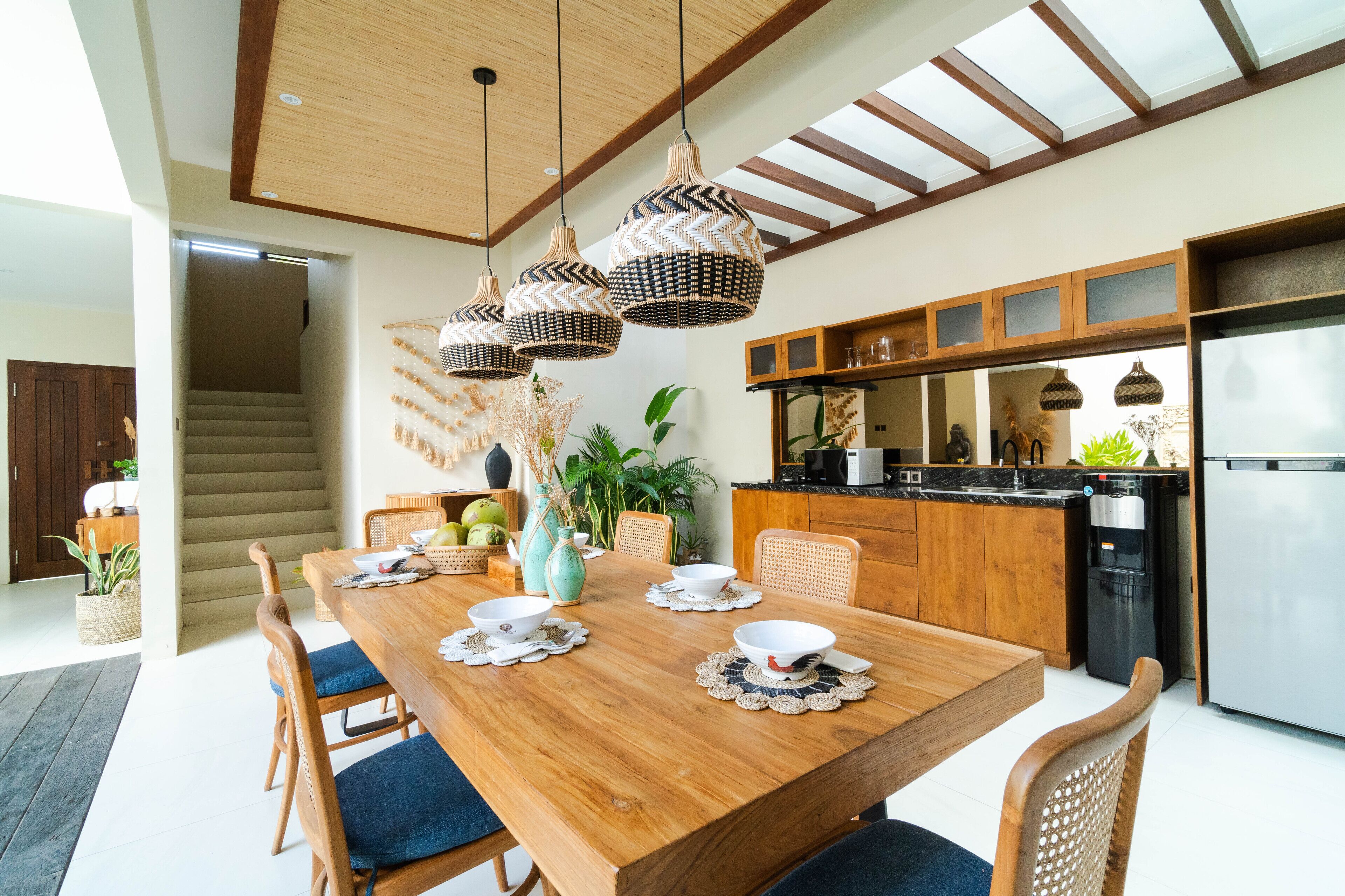 A modern kitchen with wooden cabinets, a stainless steel refrigerator, and a dining area with a wooden table and chairs.