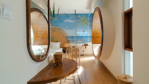 Una habitación de hotel moderna con suelo de madera, una mesa de comedor redonda y un mural con motivos playeros en la pared.