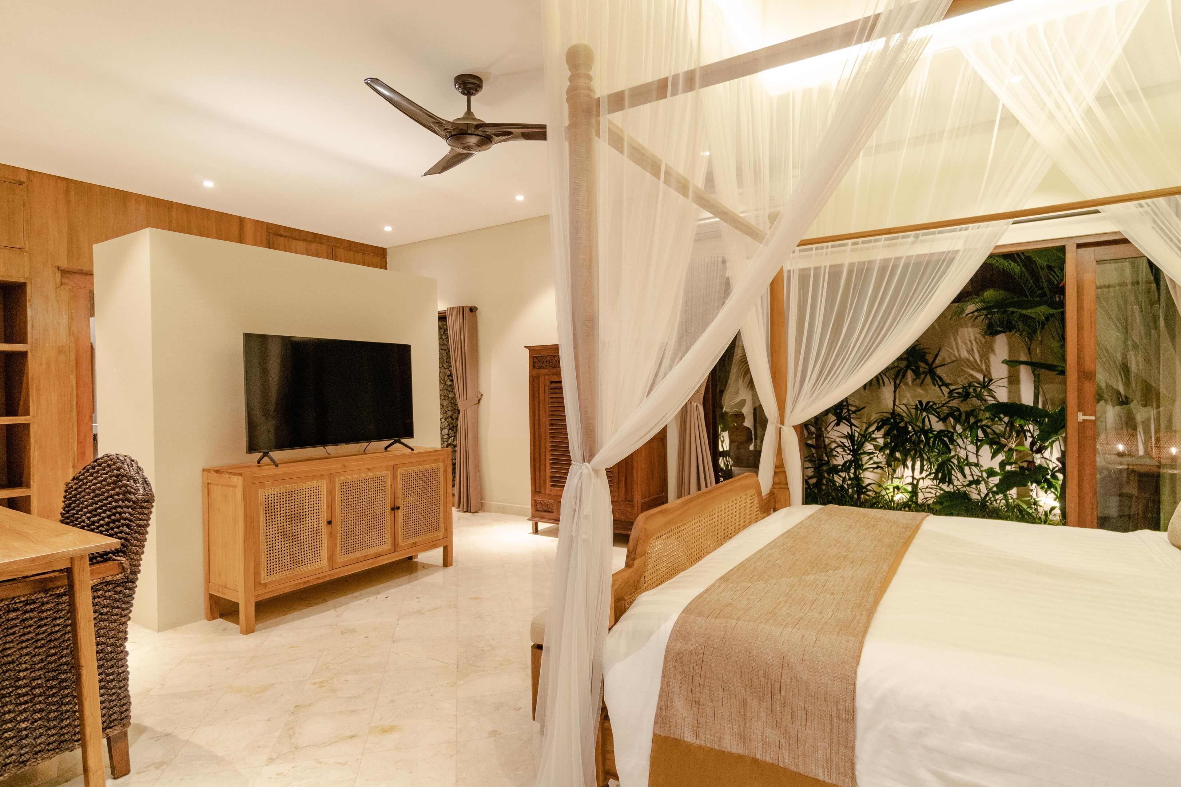 A bedroom with a bed, a TV, a wooden cabinet, and a ceiling fan.