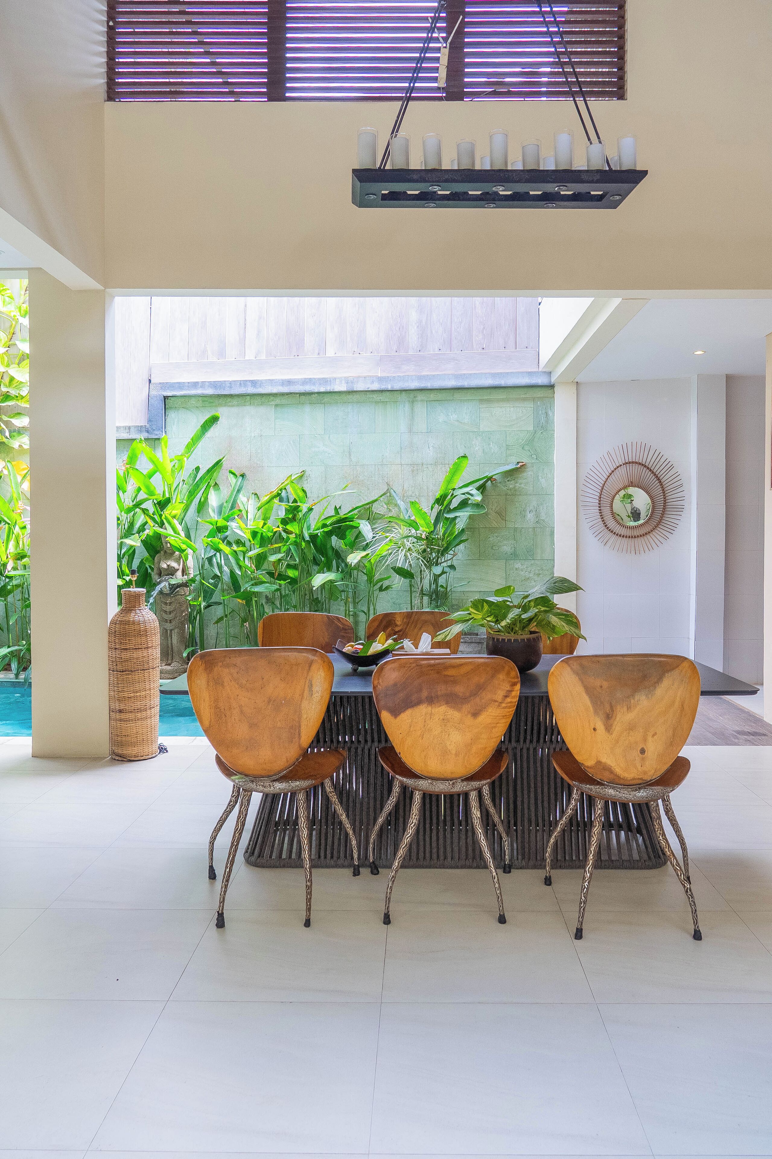 A dining area with a table and four chairs, surrounded by potted plants and a decorative wall piece.
