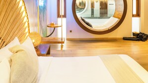 Una habitación de hotel moderna con una cama grande, un espejo circular, un sillón colgante y un mural de palmeras.