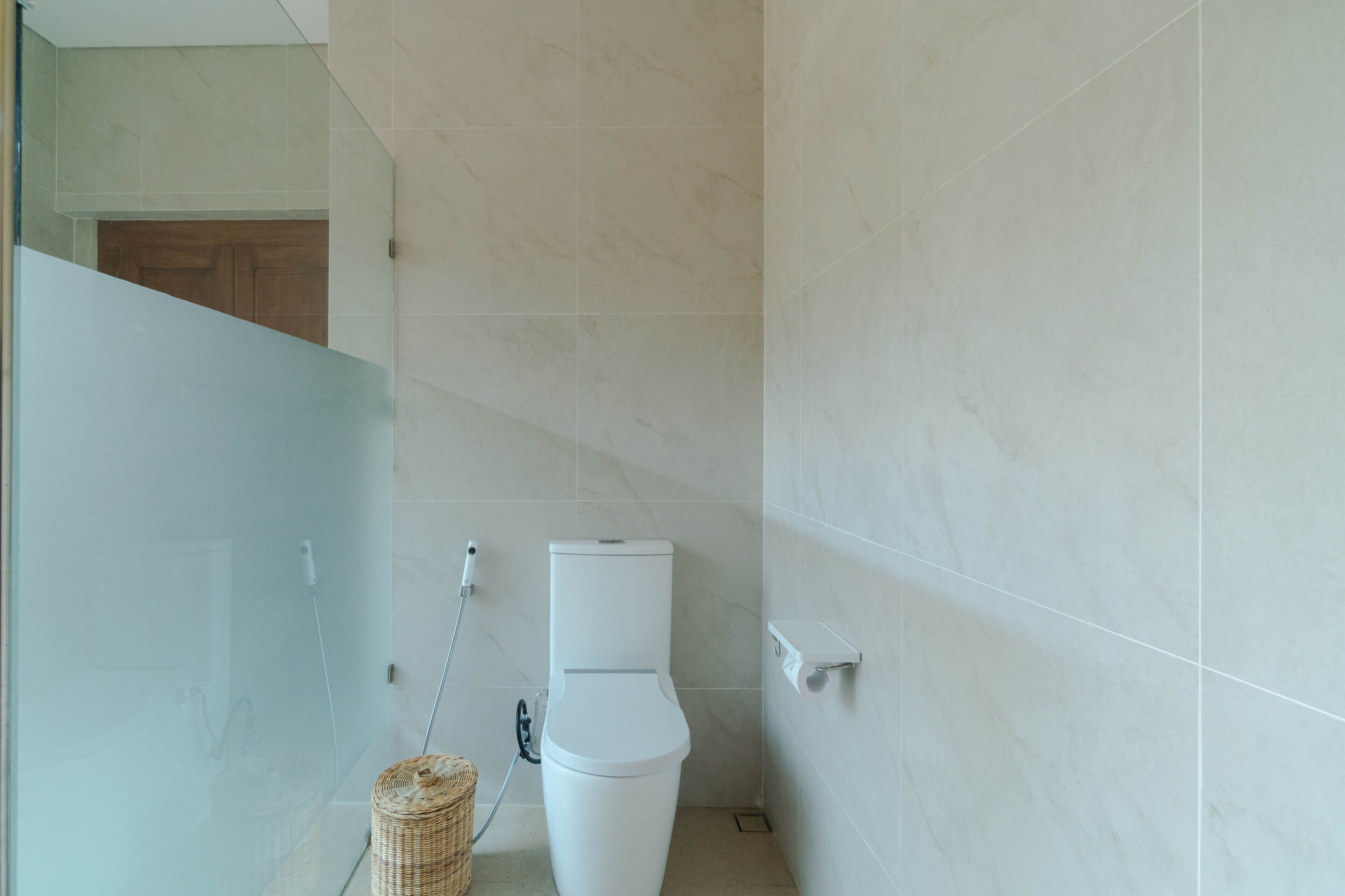 A small, modern bathroom with a toilet, a glass shower enclosure, and a tiled floor.