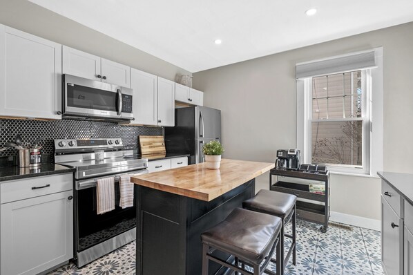 A modern kitchen with stainless steel appliances, a wooden island, and a window with blinds.