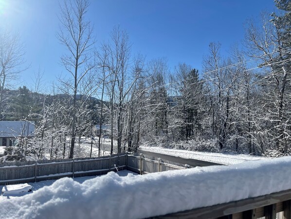 A snowy landscape with a wooden deck and a view of a house and trees.