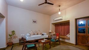 A living room with a sofa, two chairs, a coffee table, a ceiling fan, and a potted plant. - Sariska Courtyard by Armr Hospitality (Rajgarh)