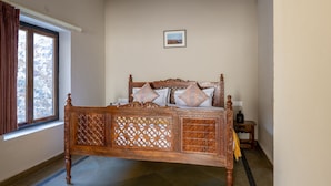 A bedroom with a wooden bed, a ceiling fan, and a window with curtains. - Sariska Courtyard by Armr Hospitality (Rajgarh)