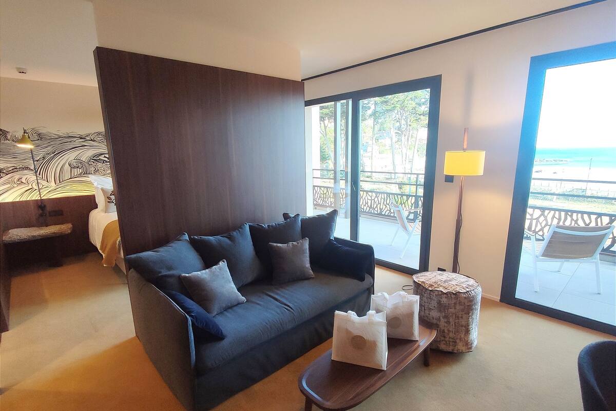A modern living room with a dark-colored sofa, a small wooden coffee table, and a view of the ocean through large sliding doors.
