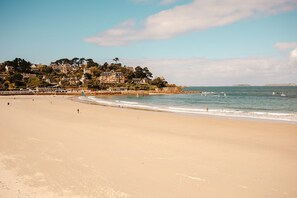 A wide sandy beach with gentle waves, a few people, and a coastal town with buildings in the background. - ROZ MARINE THALASSO RESORT (Perros-Guirec)