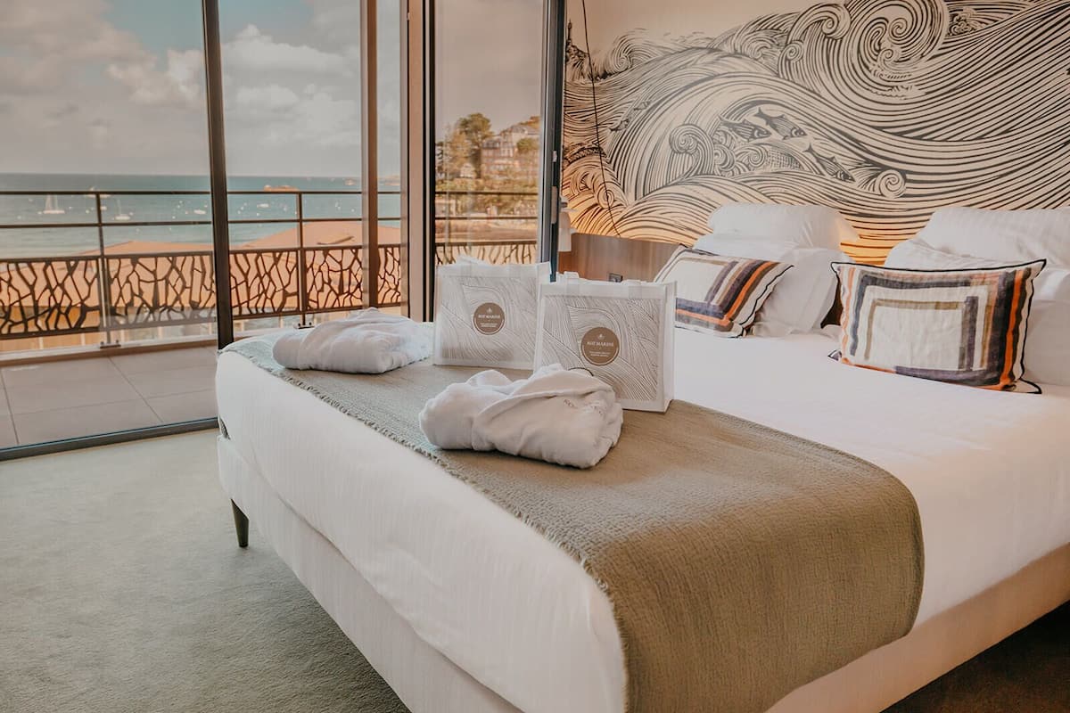 A hotel room with a large bed, a view of the sea, and a decorative wall.