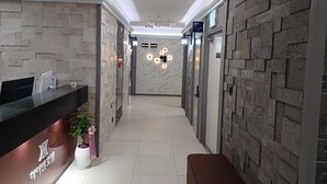 A hotel reception area with a marble wall, a reception desk, a potted plant, and a bench. - Hi&Hotel (Pyeongtaek)