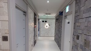 A modern hallway with a marble wall, a light fixture, and a door with a sign. - Hi&Hotel (Pyeongtaek)