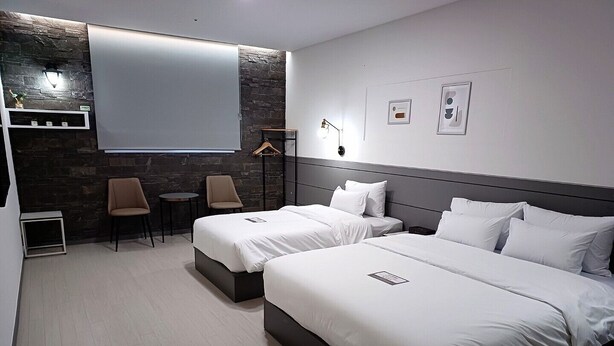 A modern hotel room with two beds, a small seating area, and a stone accent wall. - Hi&Hotel (Pyeongtaek)