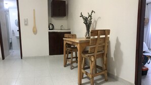 Un coin repas avec une table et des chaises en bois, un vase rempli de fleurs et, au fond, une cuisine.