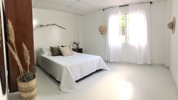 Une chambre à coucher avec un lit, une table de chevet, une fenêtre avec des rideaux et une lampe fixée au mur.