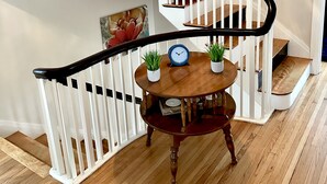 A wooden staircase with white railings, a round wooden table with two potted plants, and a clock. - Historic Brick Colonial w/Amazing Kitchen- Close to downtown (Omaha)