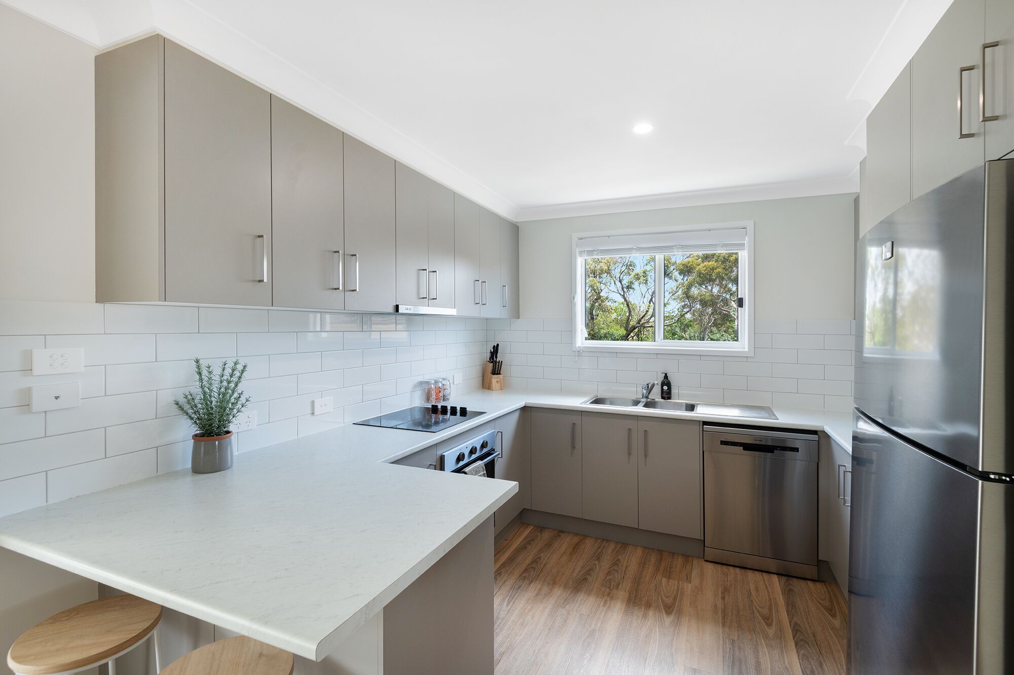 Una cocina moderna con gabinetes grises, un refrigerador de acero inoxidable y una ventana que deja entrar luz natural.