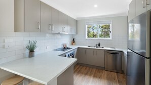 A modern kitchen with grey cabinets, a stainless steel refrigerator, and a window providing natural light.