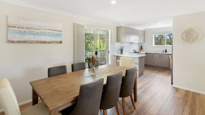A modern kitchen with white cabinets, a wooden dining table, and a view of the outdoors.