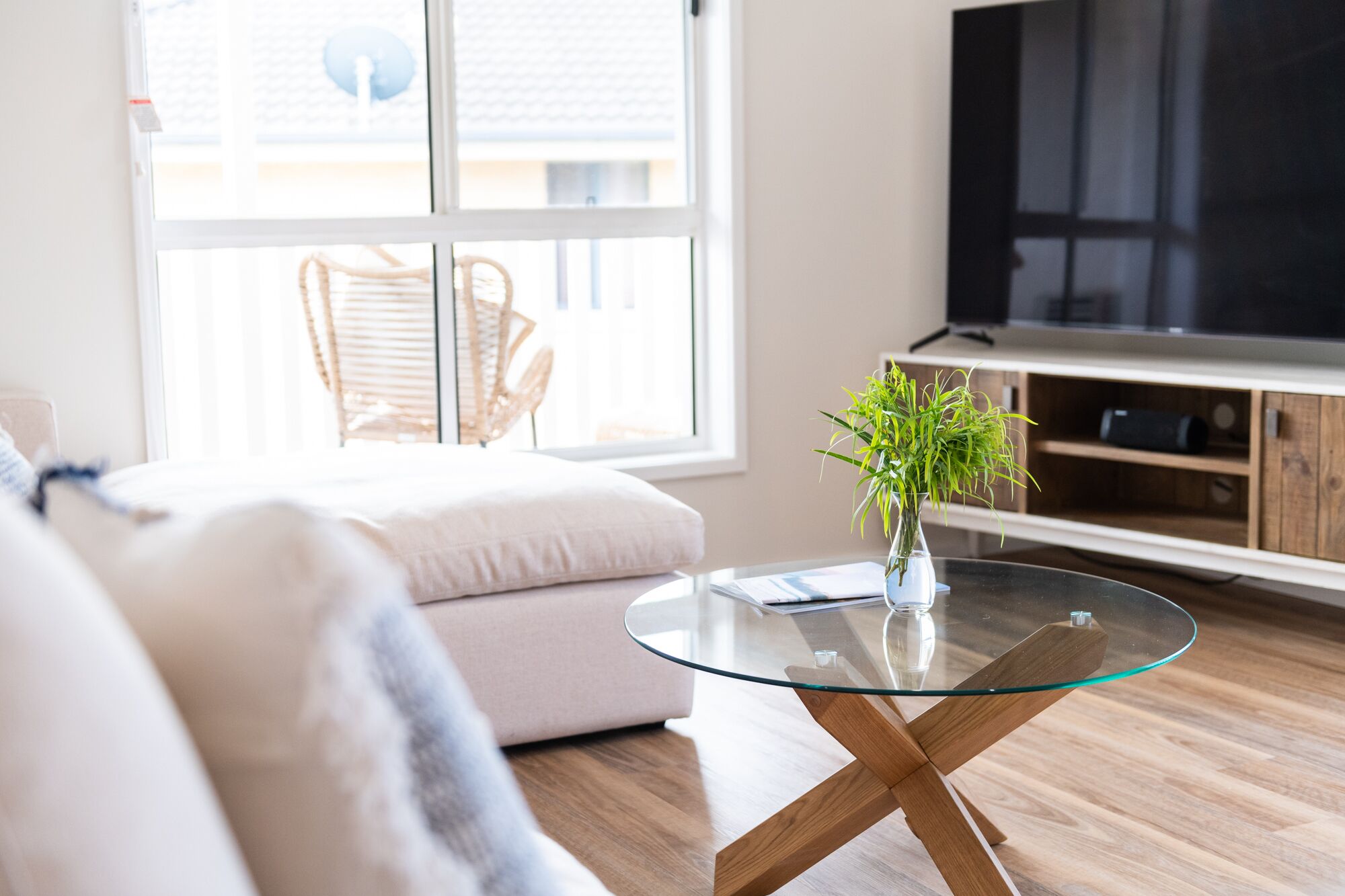 A modern living room with a glass coffee table, a sofa, a TV, and a wooden cabinet.