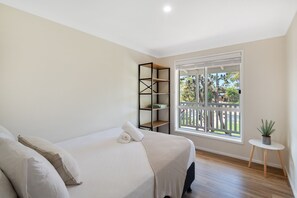 Enjoy a peaceful retreat with a garden view from this serene bedroom featuring a comfortable bed, a stylish shelving unit, and a cozy reading nook.