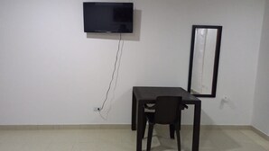 Una habitación con una televisión de pantalla plana montada en la pared, una mesa con una silla y un cuadro enmarcado.