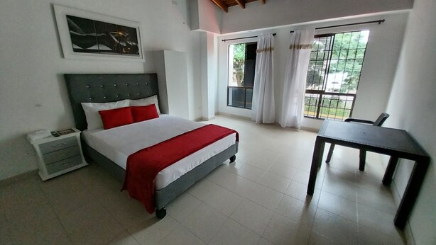 Un dormitorio con cama, mesita de noche, una mesa y un ventanal con cortinas.