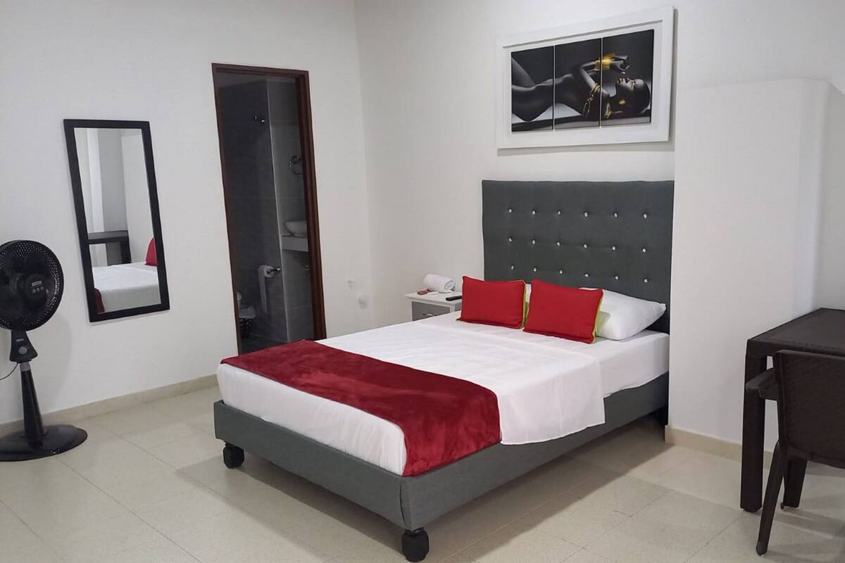 Habitación de hotel con cama, escritorio, silla, espejo y un cuadro en la pared.