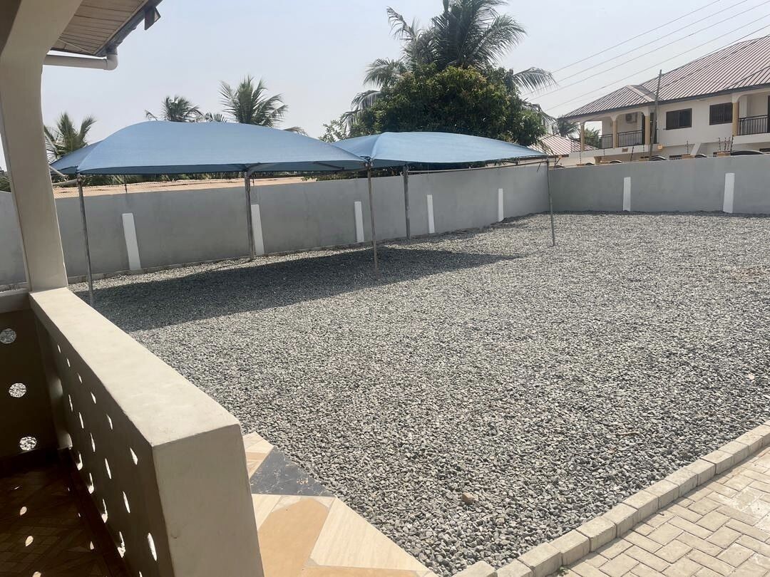 Un espacio al aire libre cubierto con suelo de grava, un muro de concreto y un edificio al fondo.