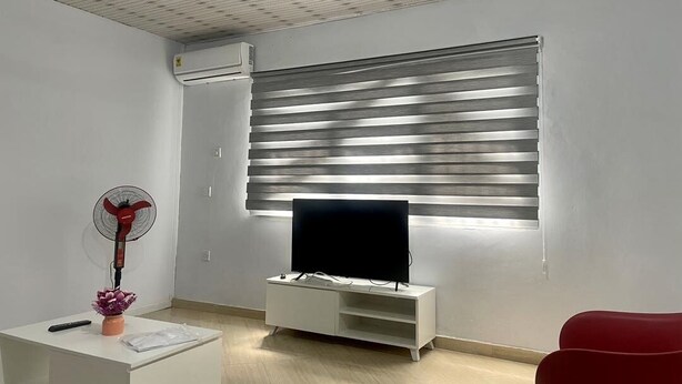 Ein modernes Wohnzimmer mit einem Flachbildfernseher auf einem weißen Standfuß, einem roten Ventilator und einem roten Sessel.