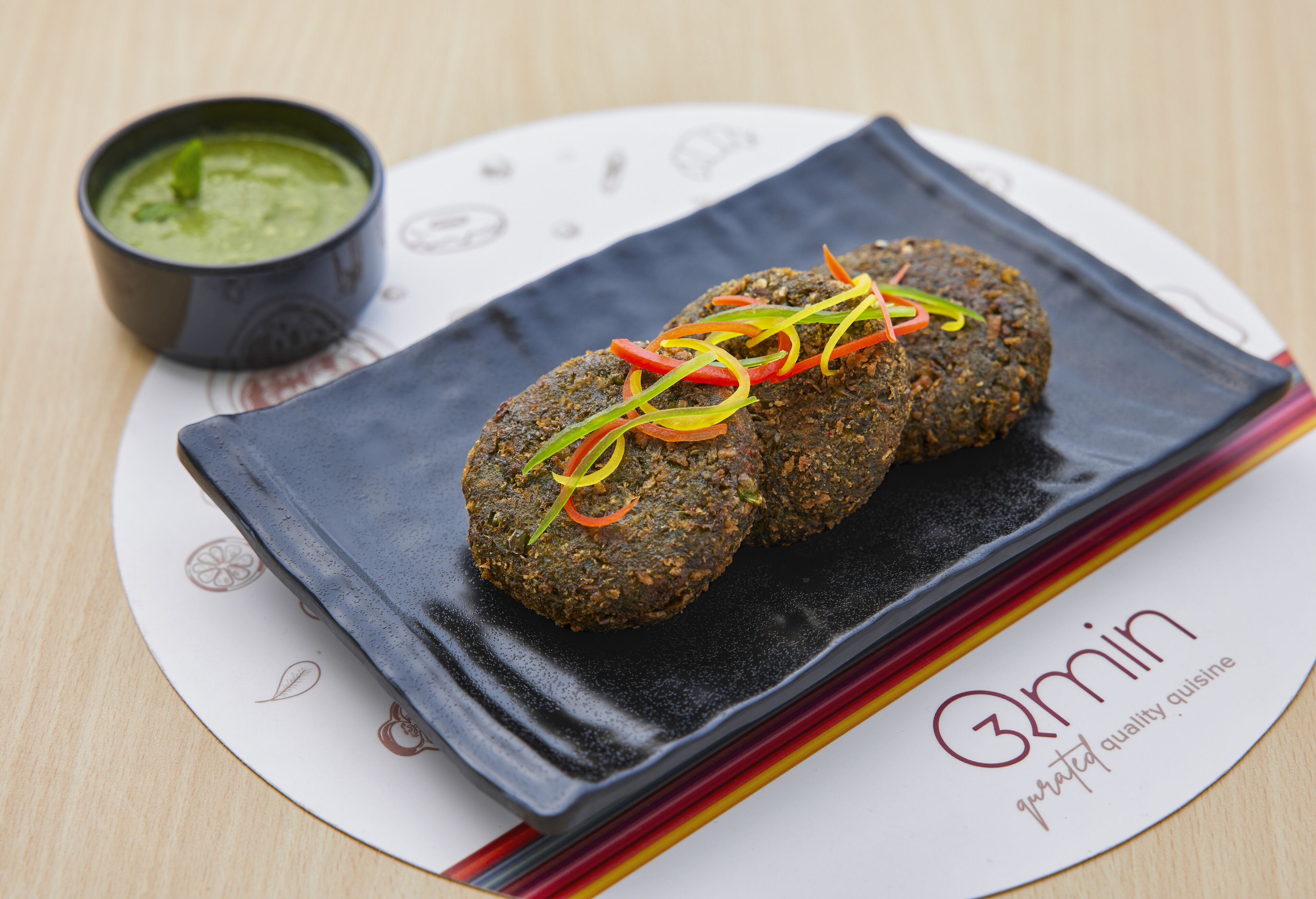 A plate with falafel balls and a green sauce, placed on a table with a placemat.