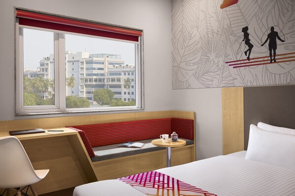 A hotel room with a large window, a desk, a bench, and a bed. - Ginger Chennai OMR (Tirupporur)