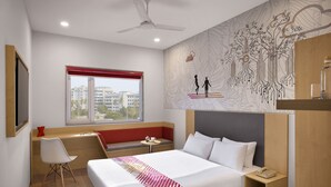 Una habitación de hotel moderna con una cama grande, un escritorio, una silla, una mesita, una mesita de noche y una ventana con una persiana roja.