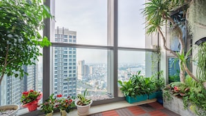 Ein Balkon mit großen Fenstern, Kübelpflanzen und Blick auf eine Stadtlandschaft.