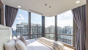 Ein modernes Schlafzimmer mit einem großen Bett, Blick auf die Stadtlandschaft durch raumhohe Fenster und einer Decke mit Einbautenbeleuchtung.
