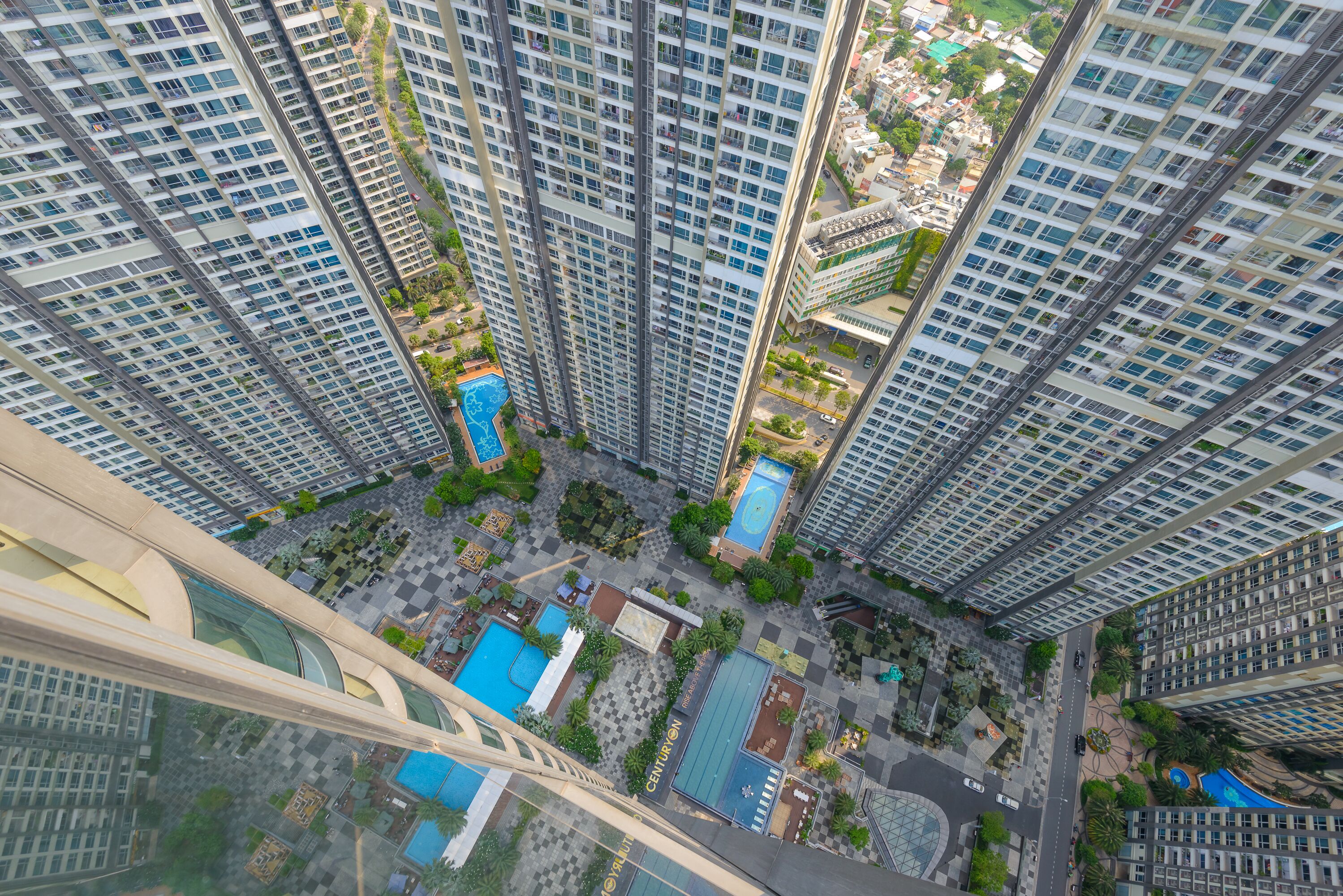 A high-rise residential building with multiple balconies, a central courtyard with a swimming pool, and surrounding greenery.