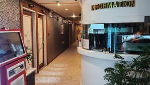 A hotel reception area with a red self-service kiosk, a reception desk labeled "INFORMATION", and a potted plant. - Hotel Hany (Daejeon)