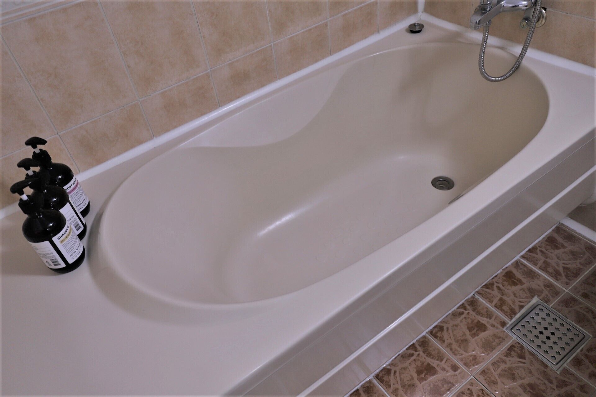 Una bañera con cabezal de ducha, una botella de champú y un desagüe.