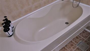 Una bañera con cabezal de ducha, una botella de champú y un desagüe.