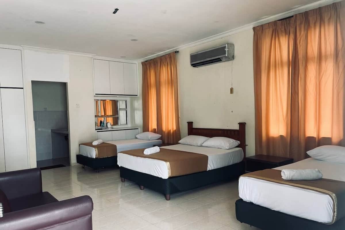 A hotel room with three beds, a kitchenette, and a seating area.