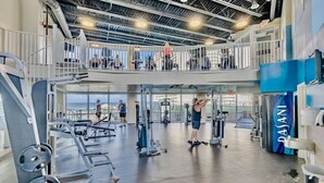 Une salle de sport à plusieurs niveaux, dotée de divers appareils d’exercice, d’une mezzanine et offrant une vue sur l’extérieur.