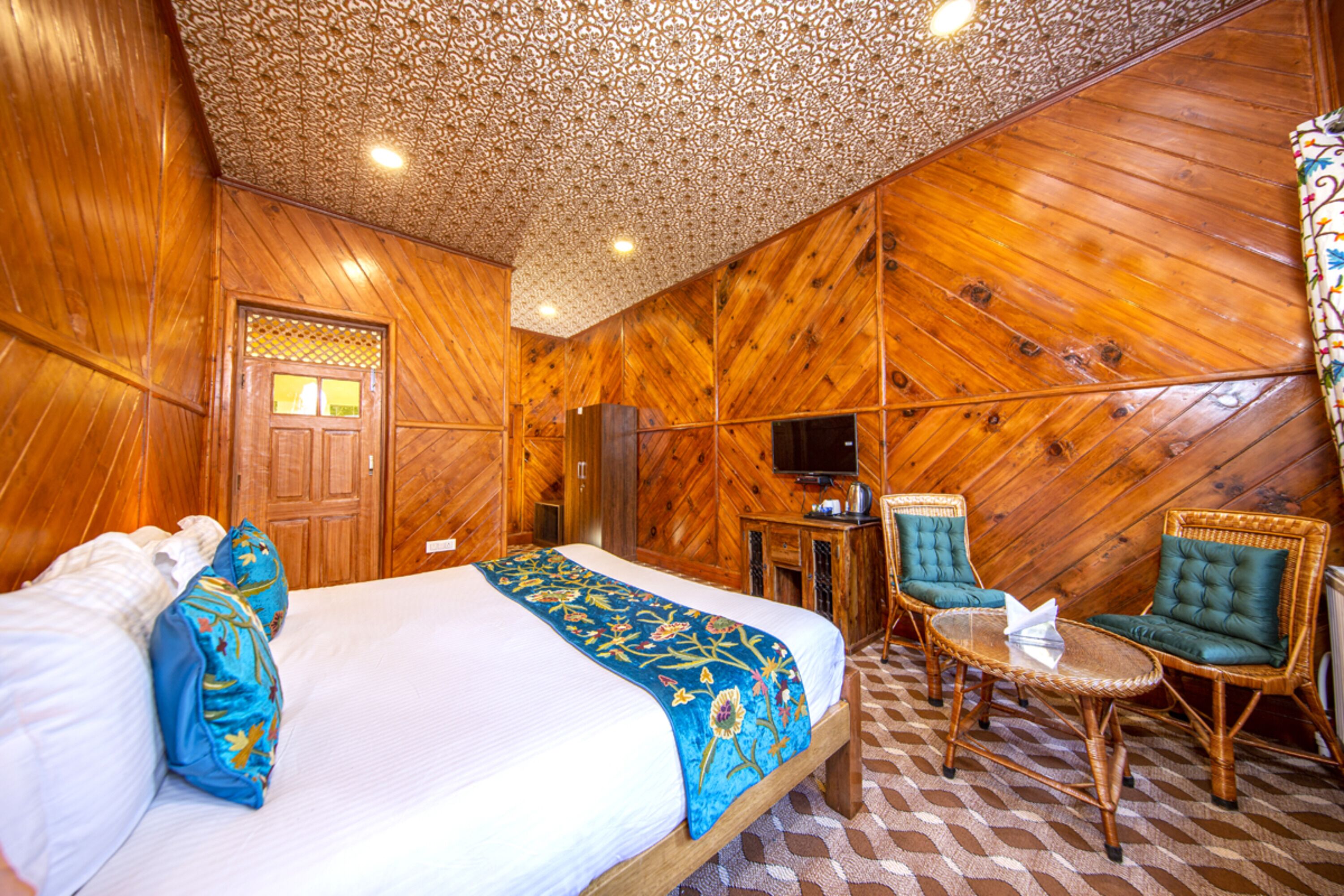 A wooden-paneled room with a bed, a television, and two wicker chairs.