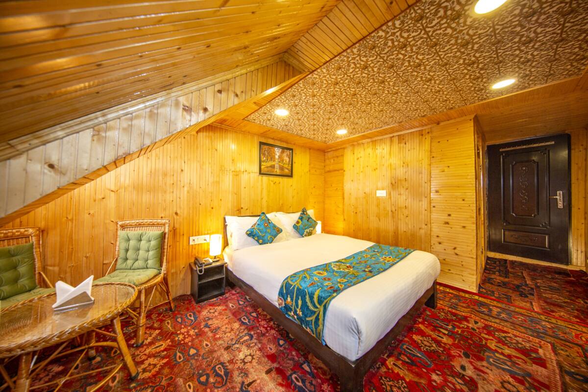Quarto de madeira com cama, cadeira, mesa de cabeceira e tapete estampado.