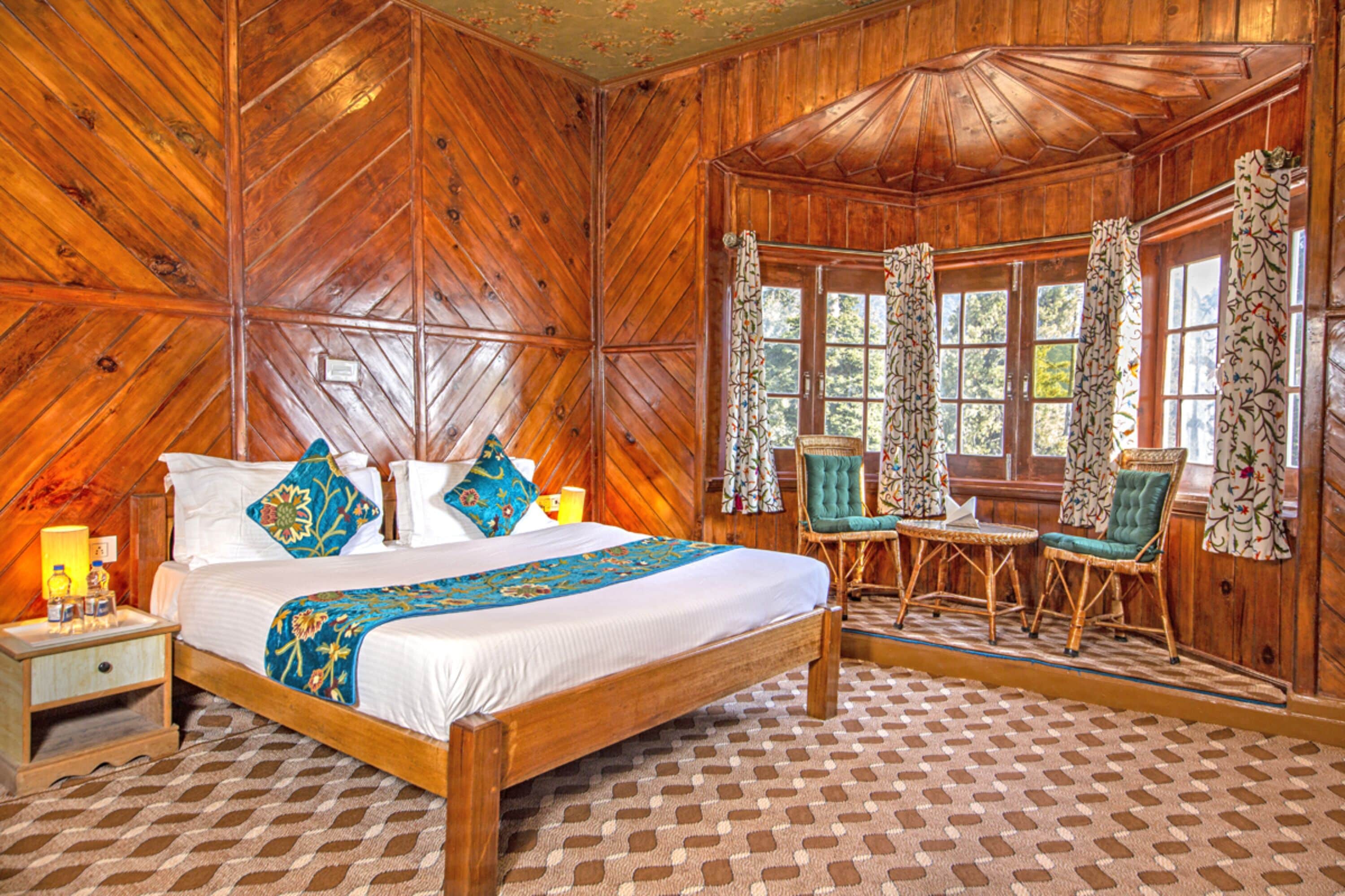 Una habitación de madera con una cama grande, dos sillas y una mesita.