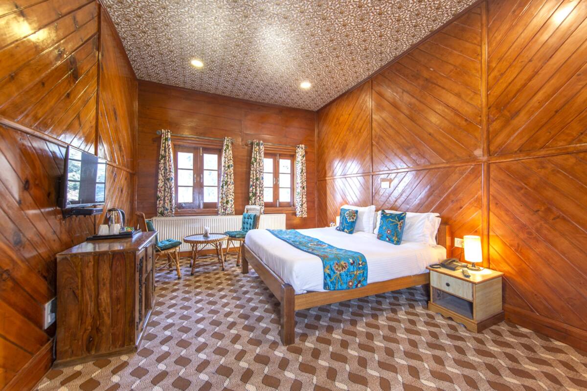 Quarto com painéis de madeira, uma cama, mesa de cabeceira e uma pequena mesa com cadeiras.