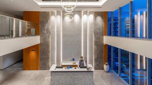 A modern reception area with a marble reception desk, a large hanging light fixture, and a view of the city through large windows. - Signature Hotels (Visakhapatnam)
