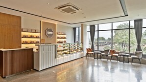 A modern cafe interior with a wooden reception desk, a glass display case of pastries, and a seating area with a view of the street. - Signature Hotels (Visakhapatnam)