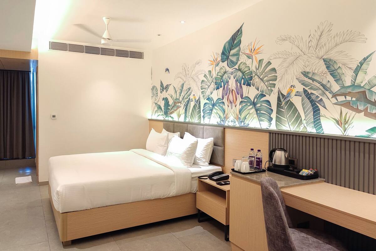 Ein Hotelzimmer mit Bett, Schreibtisch, Stuhl, Nachttisch, Wandgemälde und Deckenventilator.