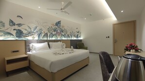 A modern hotel room with a large bed, a desk, a chair, a coffee machine, and a ceiling fan. - Signature Hotels (Visakhapatnam)