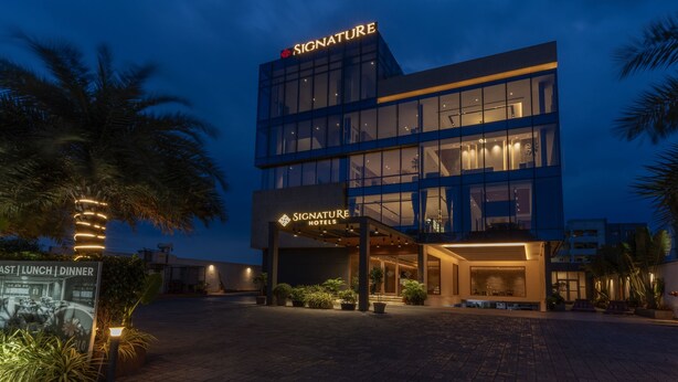 A modern hotel with a glass facade, illuminated signage, and a well-lit entrance. - Signature Hotels (Visakhapatnam)