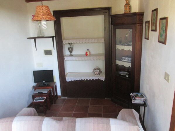 Una habitación con cama, televisión, una mesita de noche con lámpara y un armario con estantes.